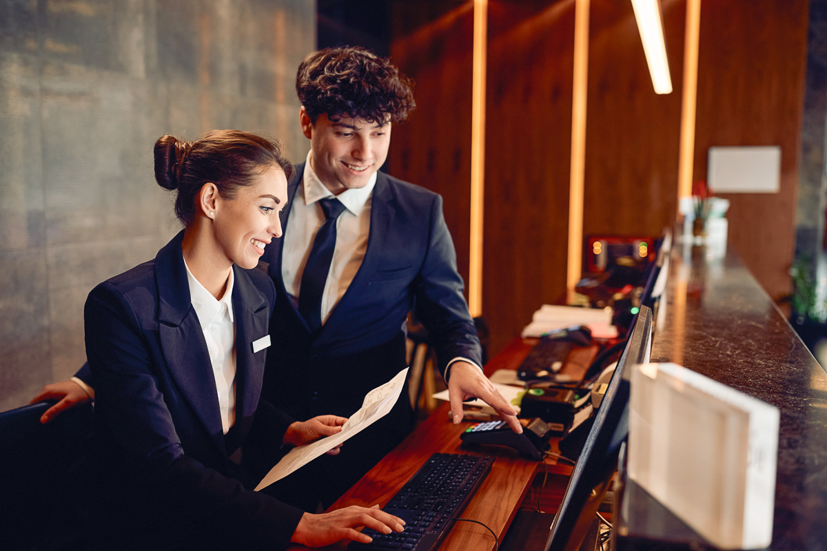 Two hotel receptionists collaborating at a computer, representing teamwork, efficient scheduling, and workforce management